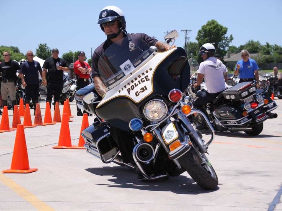 A police motor officer working a cone course while other riders and spectators watch from the edge of the range